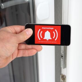Eine Hand hält eine Smarphone mit Alarmanlagen-App vor eine geöffnete Terrassentür