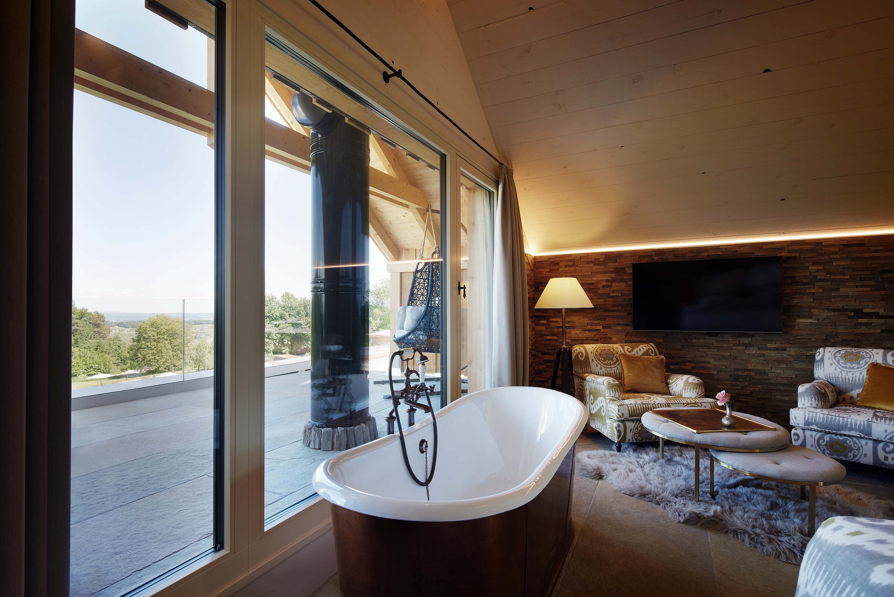 Innenansicht eines Wohnzimmers mit freistehender Badewanne vor einer Fensterfläche aus Holz-Alu