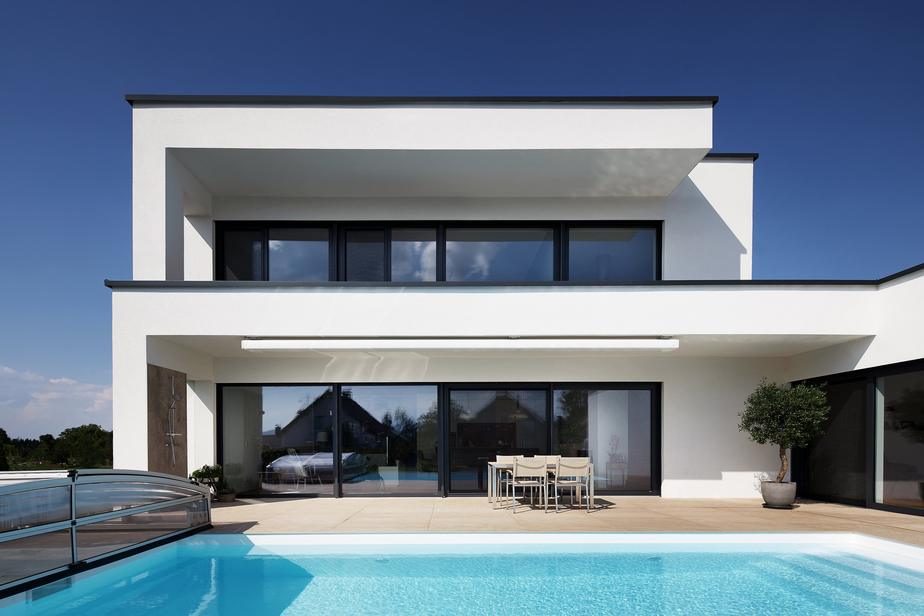 Außenansicht eines modernen zweistöckigen Wohnhauses mit Pool und dunklen Kunststoff-Aluminium-Fenstern