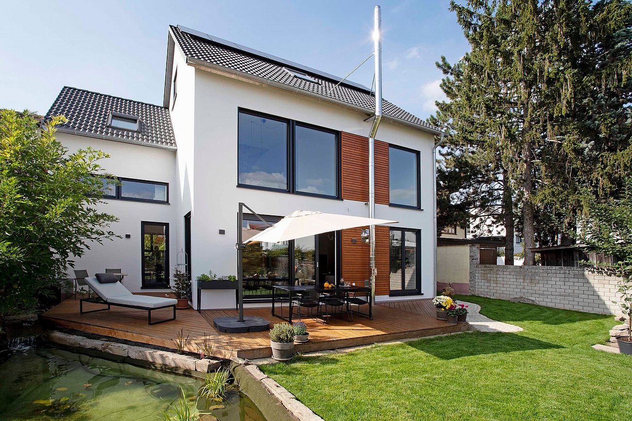 Außenansicht eines Einfamilienhauses mit Holz-Terrasse und dunklen Kunststoff-Fenstern