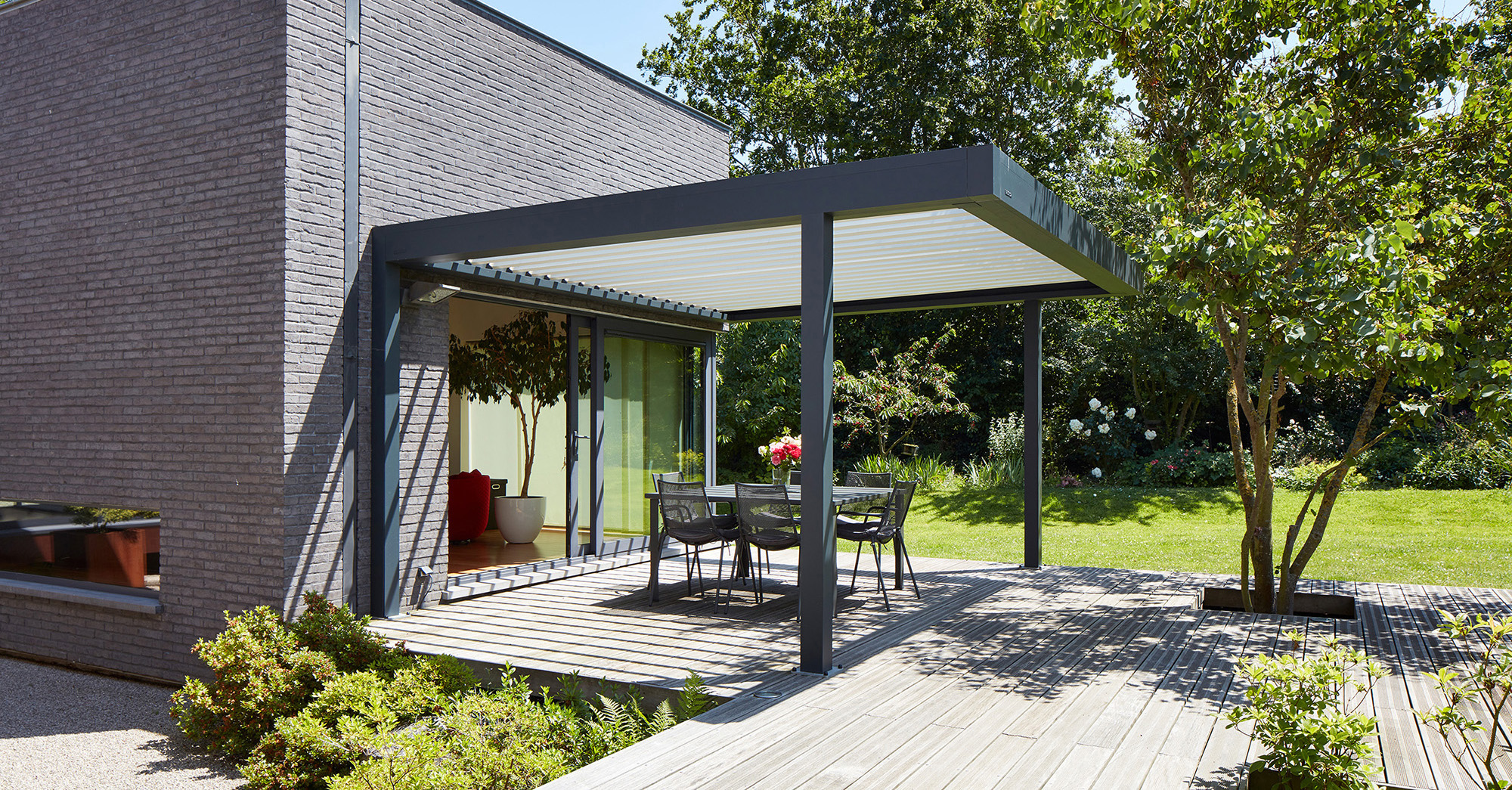 Seitlicher Blick auf eine Lamellen-Pergola als Überdachung einer großzügigen Terrasse im Grünen