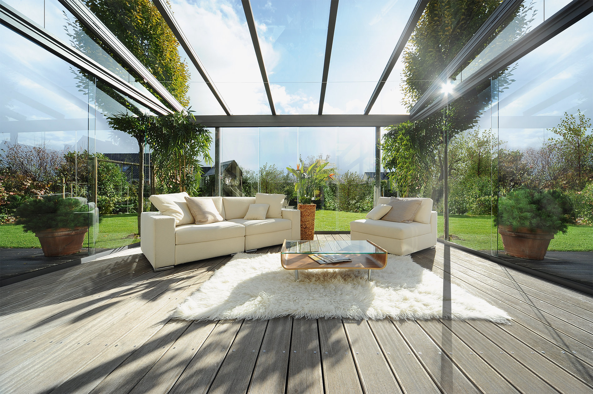 Blick über eine gemütlich eingerichtete Terrasse mit Glasdach-Pergola und verglasten Seitenwänden