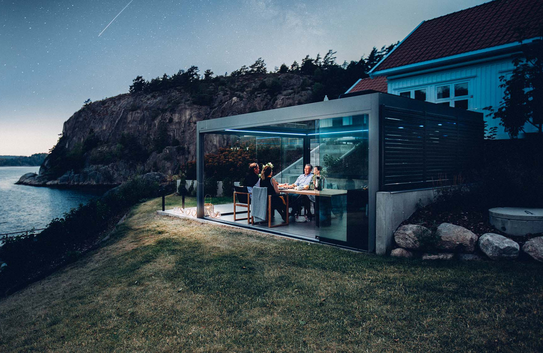 Freistehende Lamellen-Pergola mit geöffneten Seitenwänden aus Glas in der Abenddämmerung